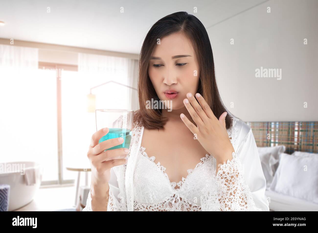 Eine Frau in einem satinweißen Nachthemd mit einem Spitzengewand fühlt sich wegen der Verwendung von Mundwasser in ihrem Mund verbrannt. Weiblich mit Gurgeln in den Morgen Weiblich U Stockfoto