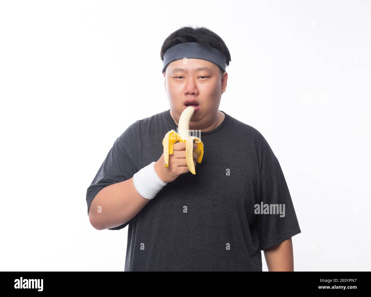 Junge asiatische lustige Fett Sport Mann Essen Banane isoliert auf weißem Hintergrund. Gesundes Lifestyle-Konzept. Stockfoto