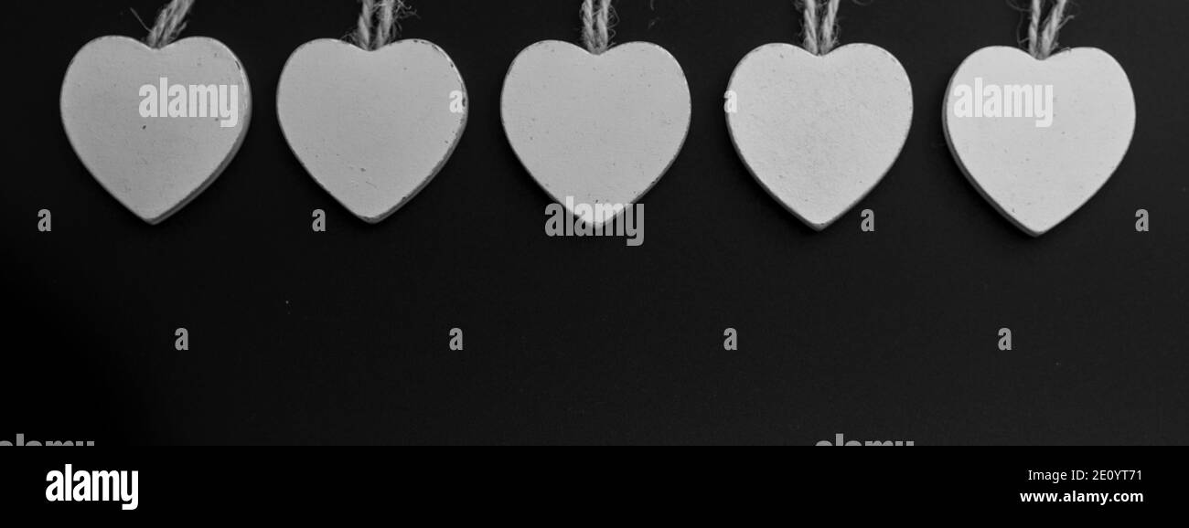 Gruppe von weißen Holzherzen auf schwarzem Hintergrund isoliert. Weiße Herzen hängen am Jute-Seil. Textur. Hintergrund. Stockfoto