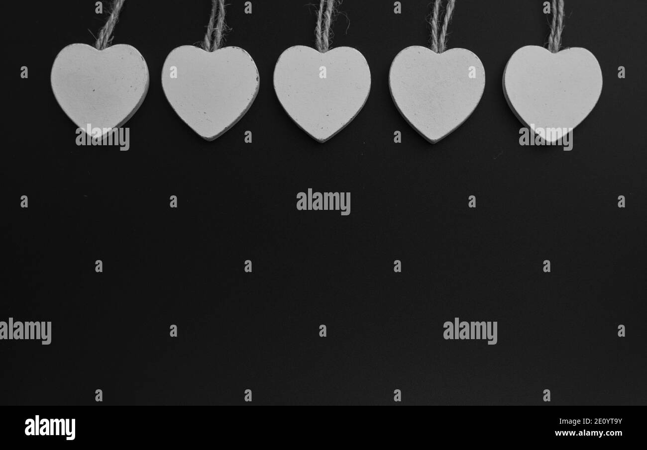 Gruppe von weißen Holzherzen auf schwarzem Hintergrund isoliert. Weiße Herzen hängen am Jute-Seil. Textur. Hintergrund. Stockfoto