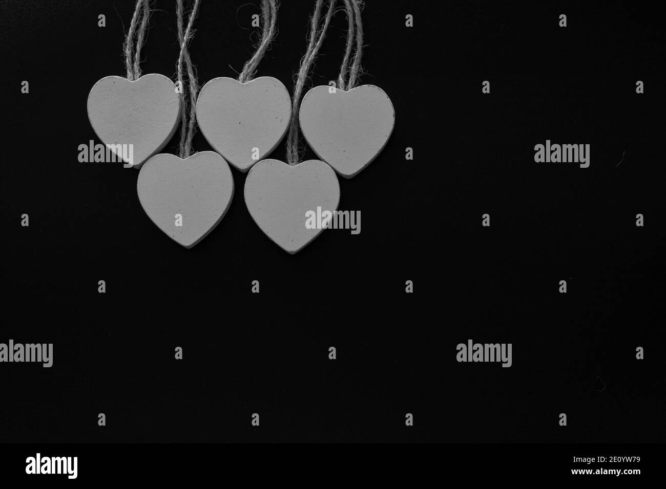 Gruppe von weißen Holzherzen auf schwarzem Hintergrund isoliert. Weiße Herzen hängen am Jute-Seil. Textur. Hintergrund. Stockfoto