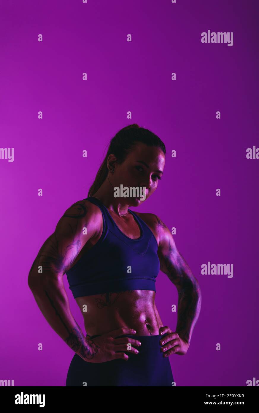 Monochromes Porträt einer muskulösen Sportlerin. Fit Frau stehen mit den Händen auf der Taille auf lila Hintergrund. Stockfoto