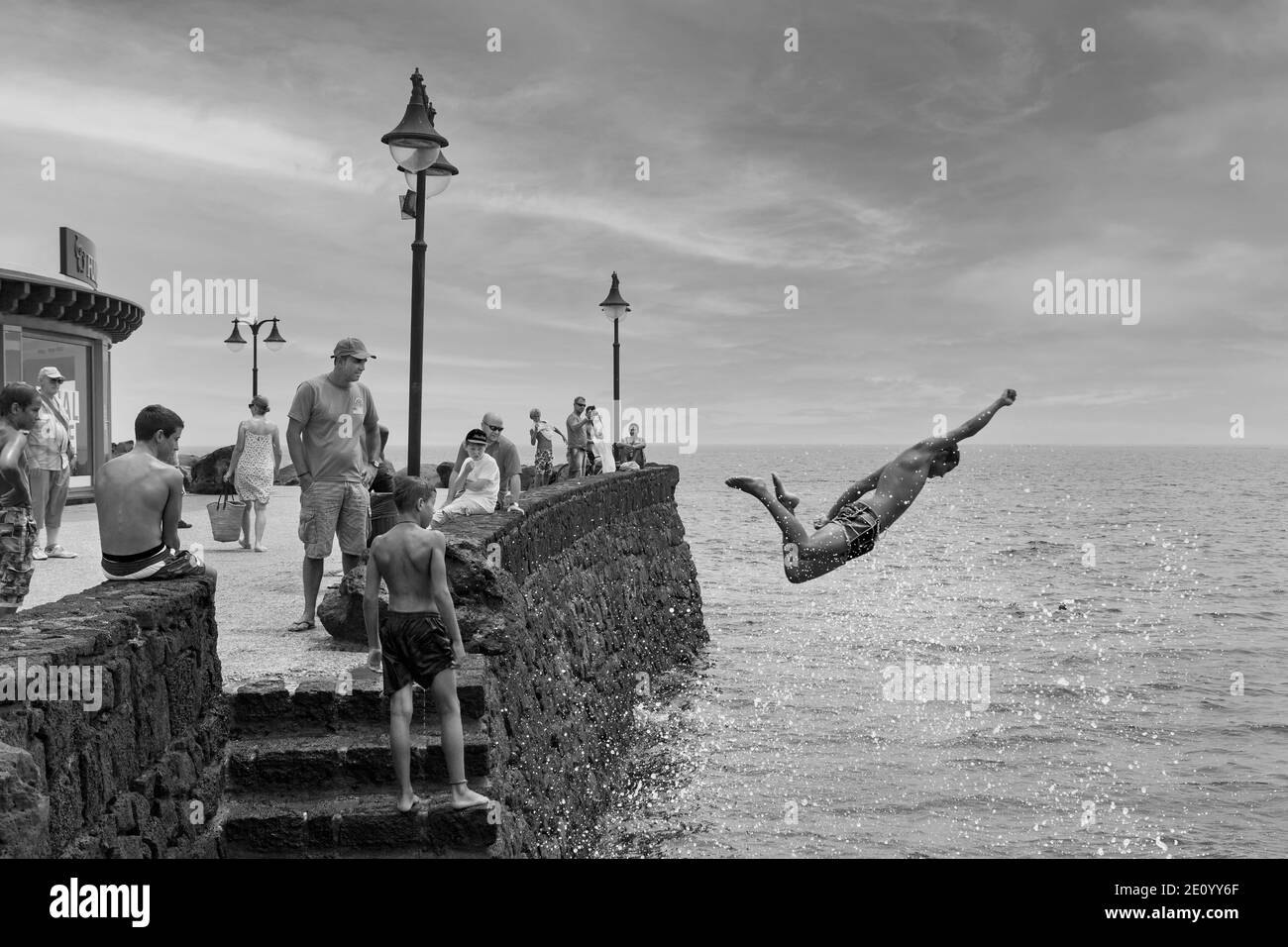 Boy springt ins Meer von der Kaimauer mit Superman-Geste Stockfoto