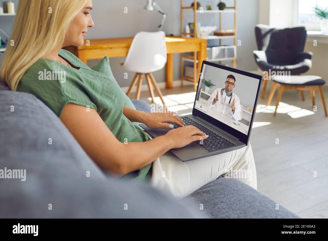 Junge Frau sitzt auf dem Sofa mit Laptop und spricht mit Online-Arzt der E-Health-Klinik Stockfoto