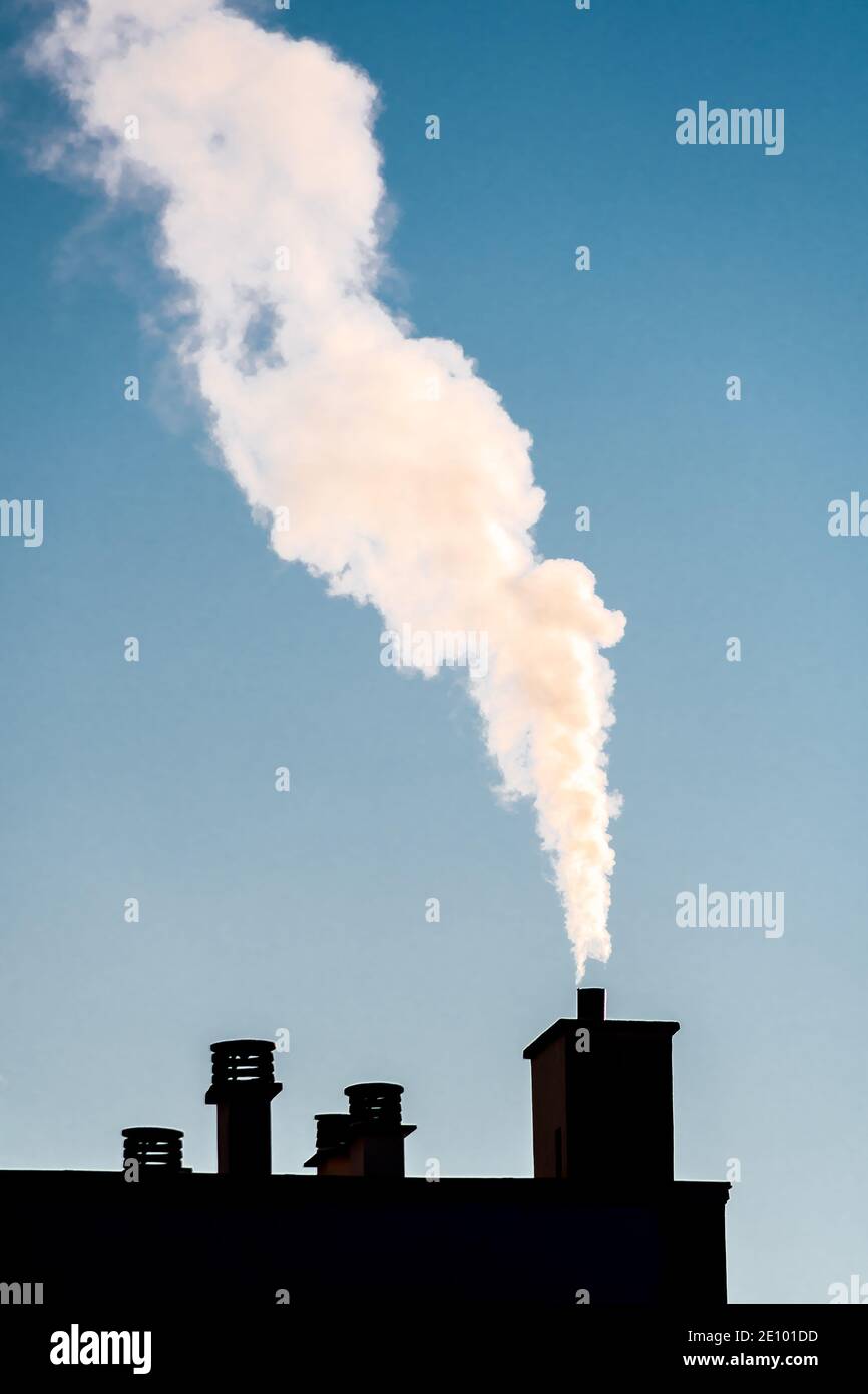 Weißer Rauch aus einem Kamin auf dem Dach eines Wohnhauses. Konzepte von Kälte, Heizung und Verschmutzung Stockfoto