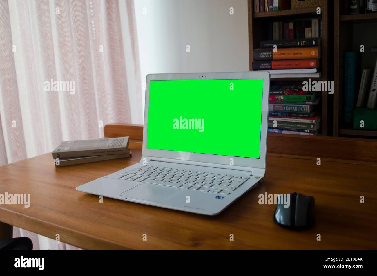 Laptop mit grünem Bildschirm auf einem Holztisch, verschwommene Bibliothek auf der Rückseite Stockfoto