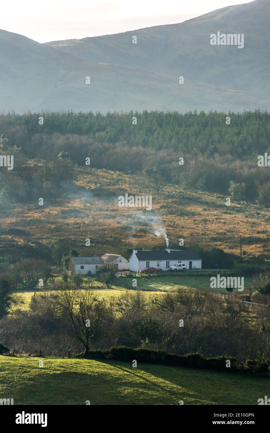 Ardara, County Donegal, Irland 3. Januar 2021. Ein Haus im ländlichen Irland mit Schornsteinrauch. Die irische Regierung plant ein landesweites Verbot des Verkaufs aller rauchigen Kraftstoffe, da sie sich weiterhin Sorgen über die gesundheitlichen Auswirkungen der Luftverschmutzung macht. Detaillierte Vorschläge werden bis Februar veröffentlicht. Zu den Brennstoffen, die verboten werden sollen, gehören Kohle, Torfbriketts, Sod-Rasen und nasses Holz. Das vorgeschlagene Verbot wird Teil der neuen Strategie der Regierung für saubere Luft sein. Kredit: Richard Wayman/Alamy Live Nachrichten Stockfoto