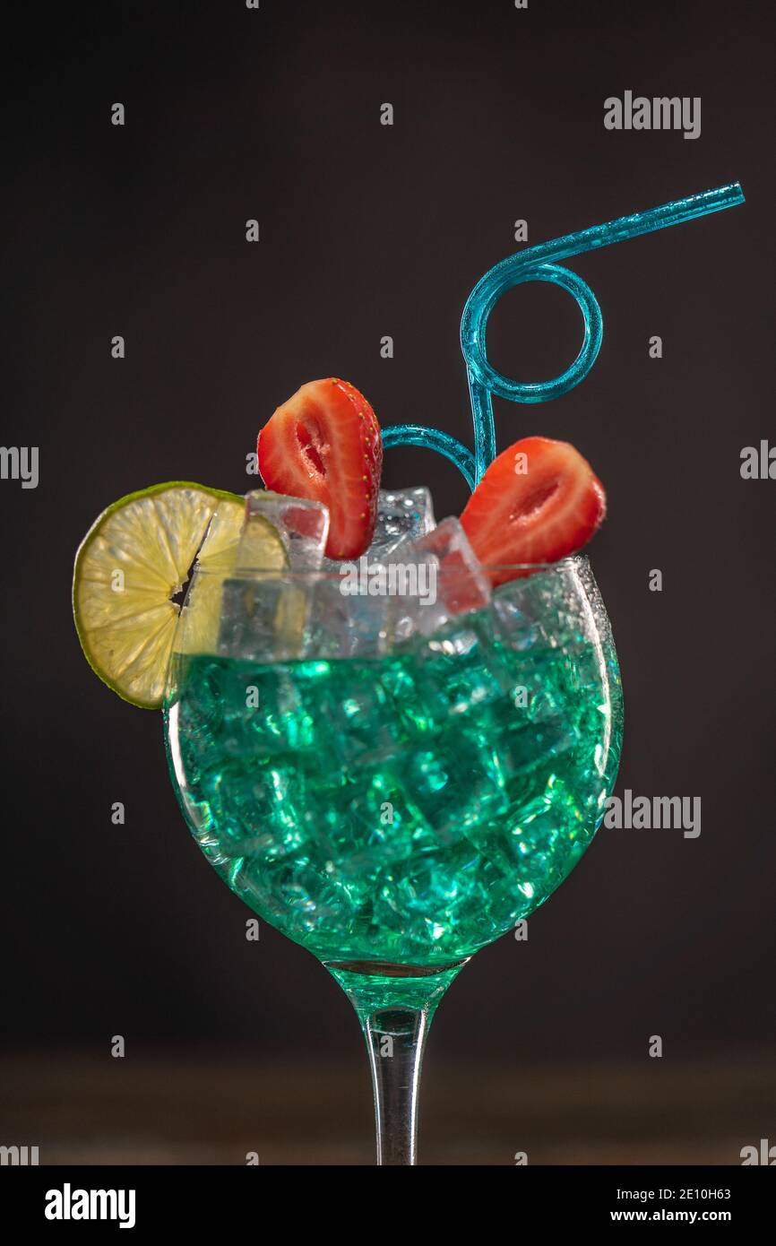 Ein smaragdfarbener Cocktail in einem Eisglas, das mit dekoriert ist Limette und Erdbeeren mit einem lockigen Trinkhalm Stockfoto