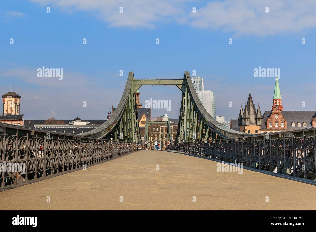 Fußgängerbrücke über den Main in Frankfurt. Eisenbrücke tagsüber mit wenigen Leuten. Häuser der Altstadt im Hintergrund mit Sonnenschein Stockfoto