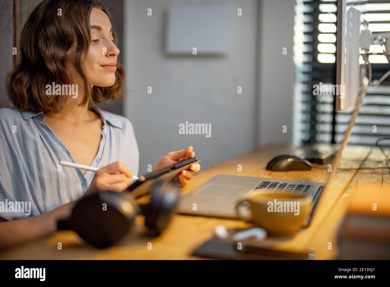 Junge Frau, die lässig gekleidet ist und kreative Arbeit hat, auf einem digitalen Tablet zeichnet und im gemütlichen und stilvollen Home Office sitzt Stockfoto