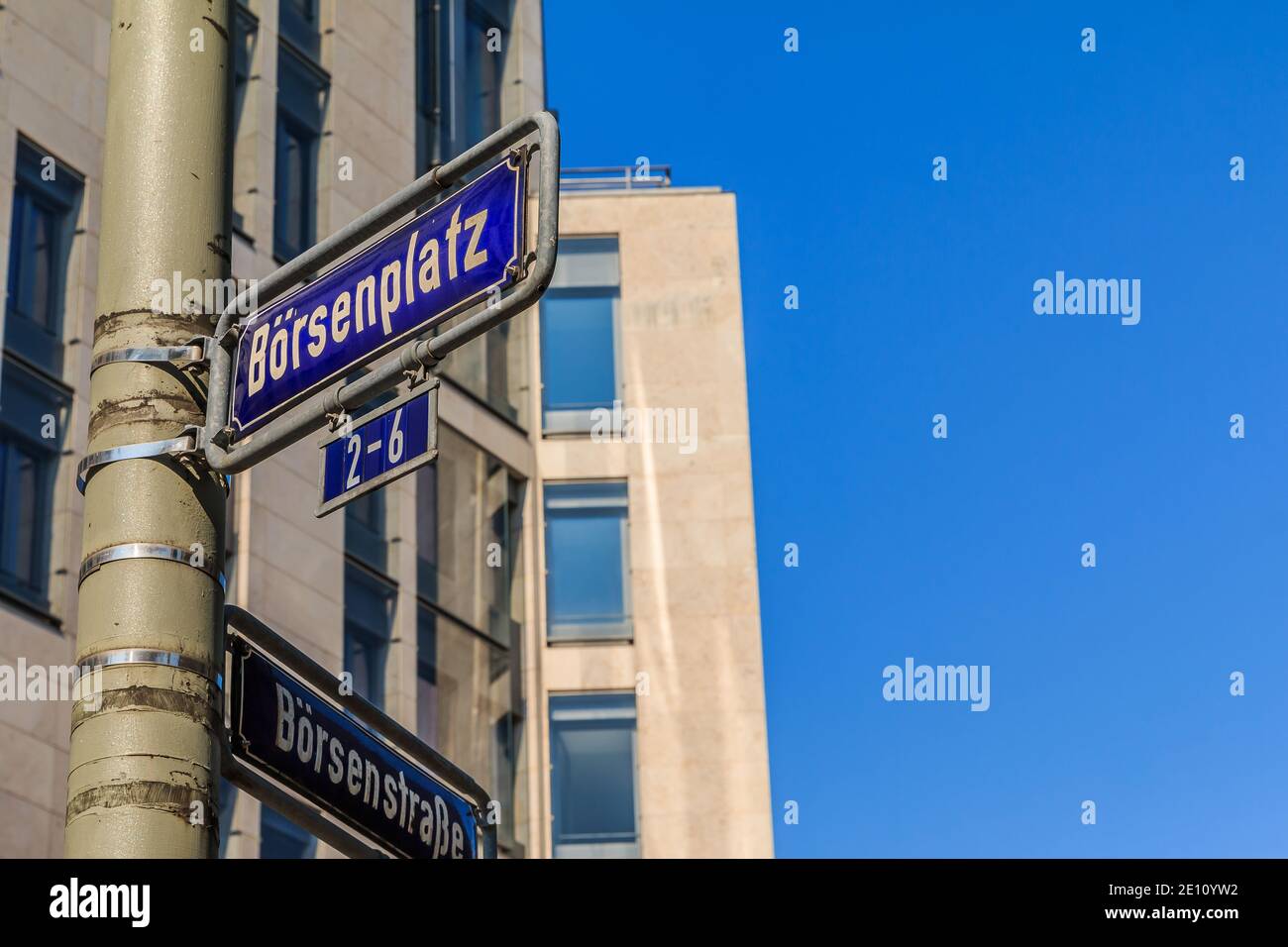 Blaues Verkehrszeichen Börsenplatz und Börsenstraße auf einer grauen Laternenpfosten mit Befestigungen. Haus mit Fensterfassade im Hintergrund mit blau Stockfoto