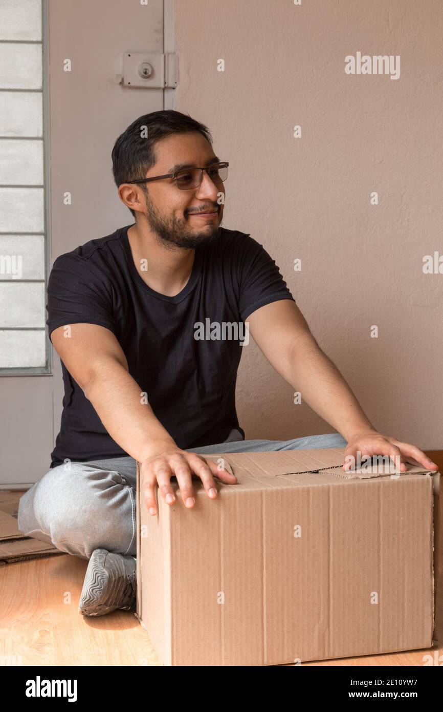 latein Mann öffnet eine Box in seiner neuen Wohnung durch Ein Fenster mit schwarzem T-Shirt und Sportswear Stockfoto