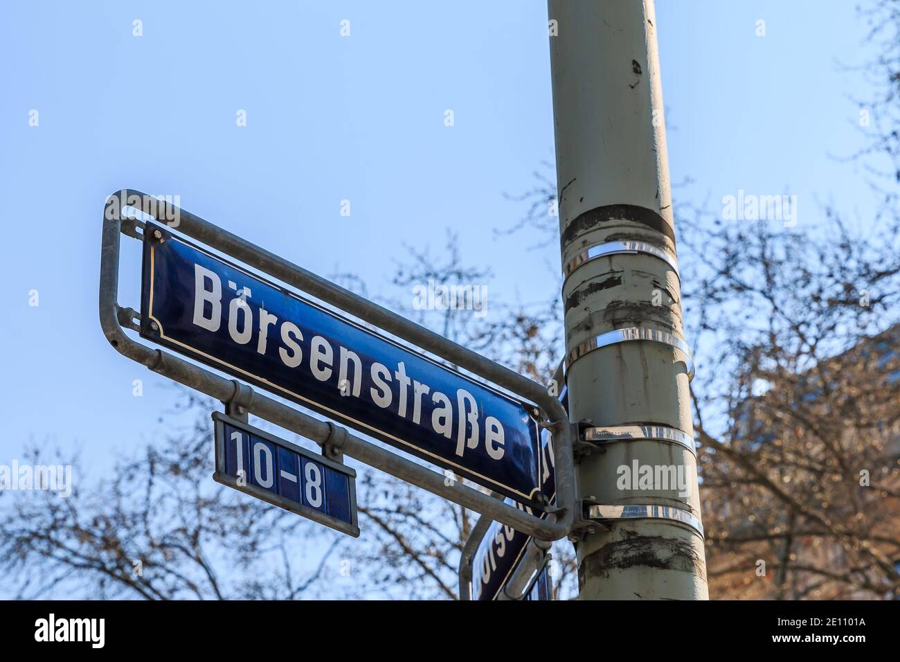 Blaue Straßenschild Börse auf einem grauen Laternenpfosten mit Befestigungen. Haus Nummer acht bis zehn auf dem Schild. Haus mit Fensterfassade und Bäumen im Frühjahr in Th Stockfoto