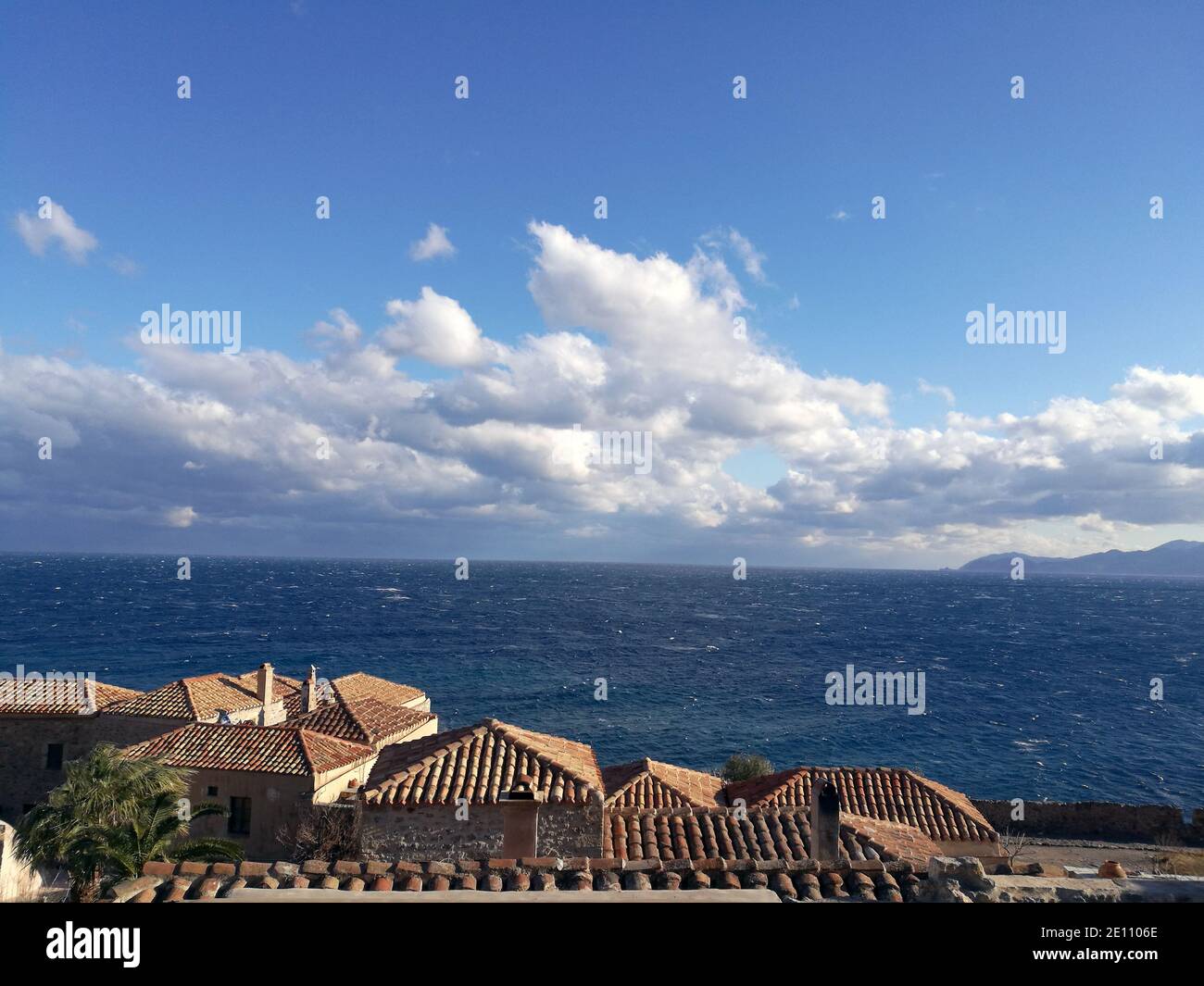 Aspekt der Ziegeldächer in der alten Zitadellenstadt Monemvassia, Griechenland, mit dem blauen Meer und Wolkenlandschaft im Hintergrund Stockfoto