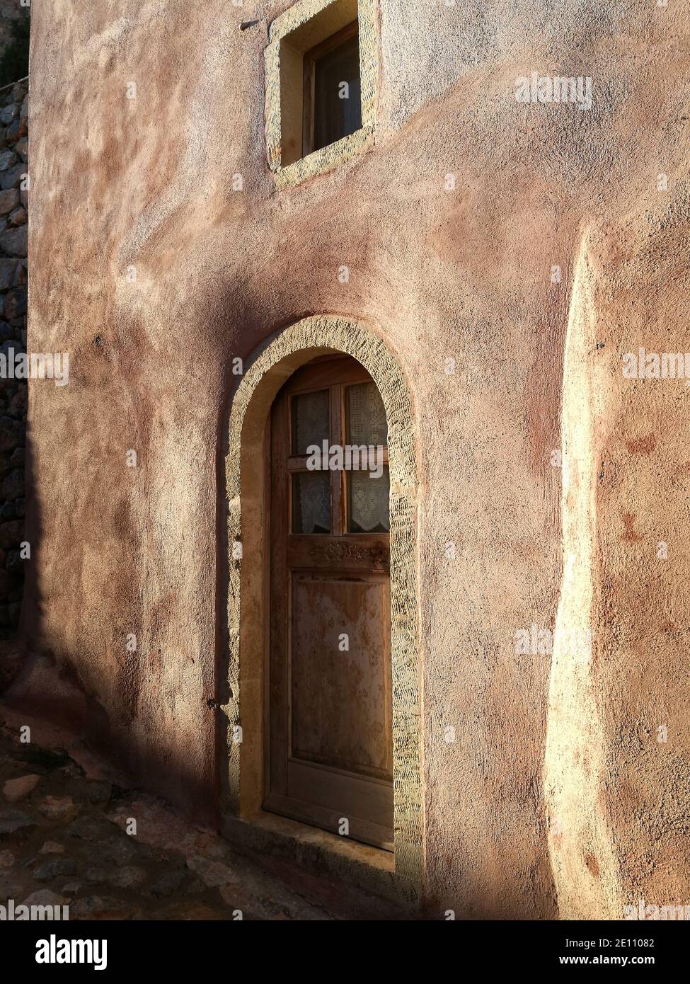 Detail einer hölzernen Tür und einer bunten strukturierten Wand eines Hauses an der alten Zitadellenstadt von Monemvassia, Griechenland, an der Morgendämmerung Stockfoto