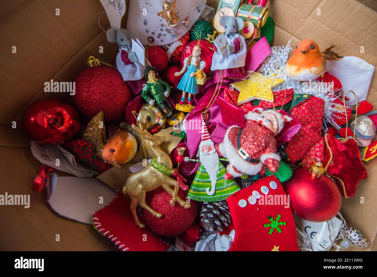 Braune Pappschachtel mit einem Durcheinander von Familie bunte Weihnachten Baumschmuck vor einem Holzbrenner auf einem Stein Boden wird weggepackt Stockfoto
