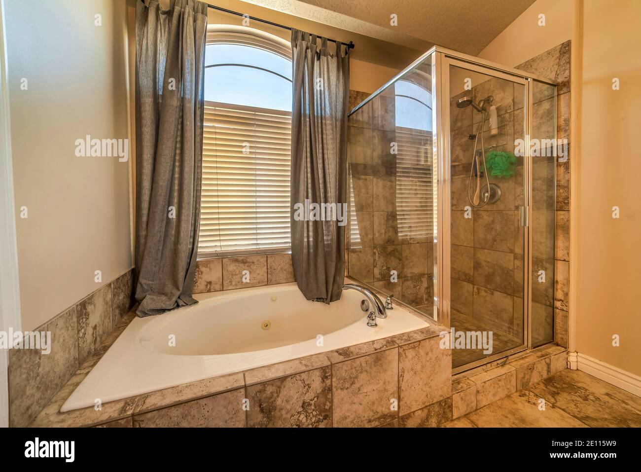 Badezimmer mit runder eingebauter Badewanne mit Duschkabine und Fliesen in warmen Farbtönen Stockfoto