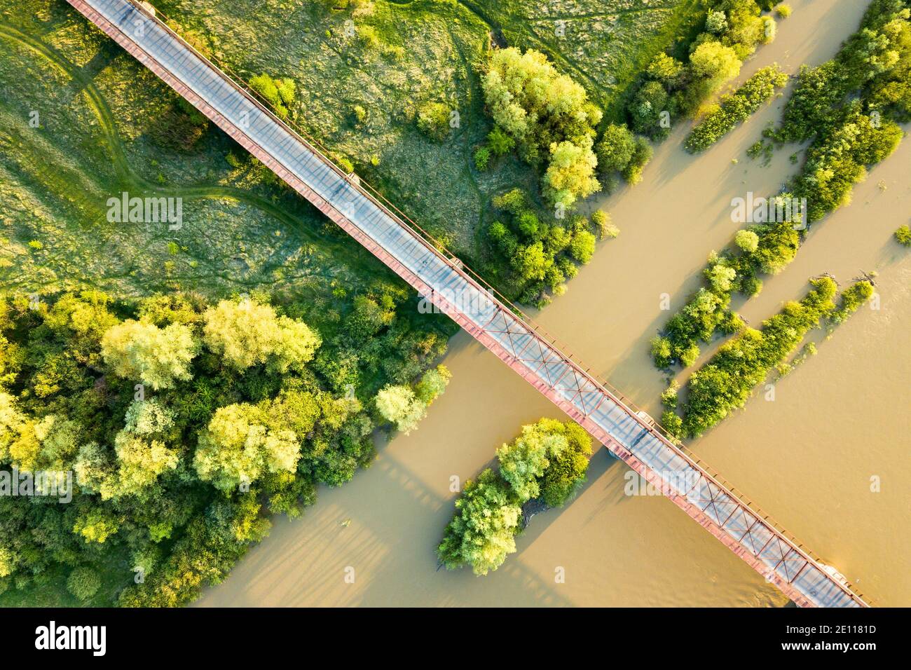 Luftaufnahme einer schmalen Straßenbrücke, die sich über einen schlammigen, breiten Fluss in grüner ländlicher Umgebung erstreckt. Stockfoto