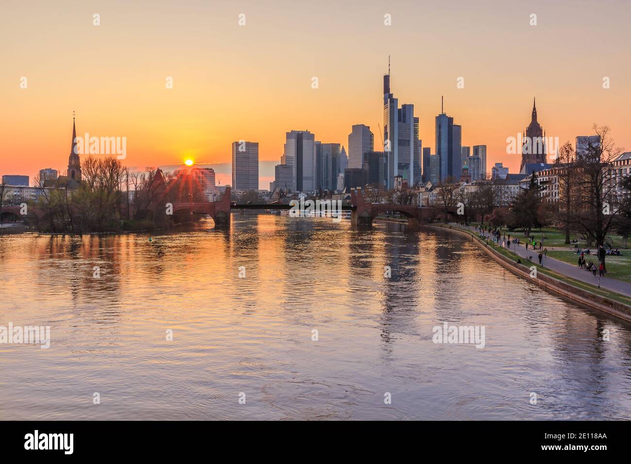 Sonnenuntergang über der Frankfurter Skyline. Wolkenkratzer, Geschäftshäuser am Horizont. Main mit Brücke und Park am Ufer. Reflexionen der s Stockfoto