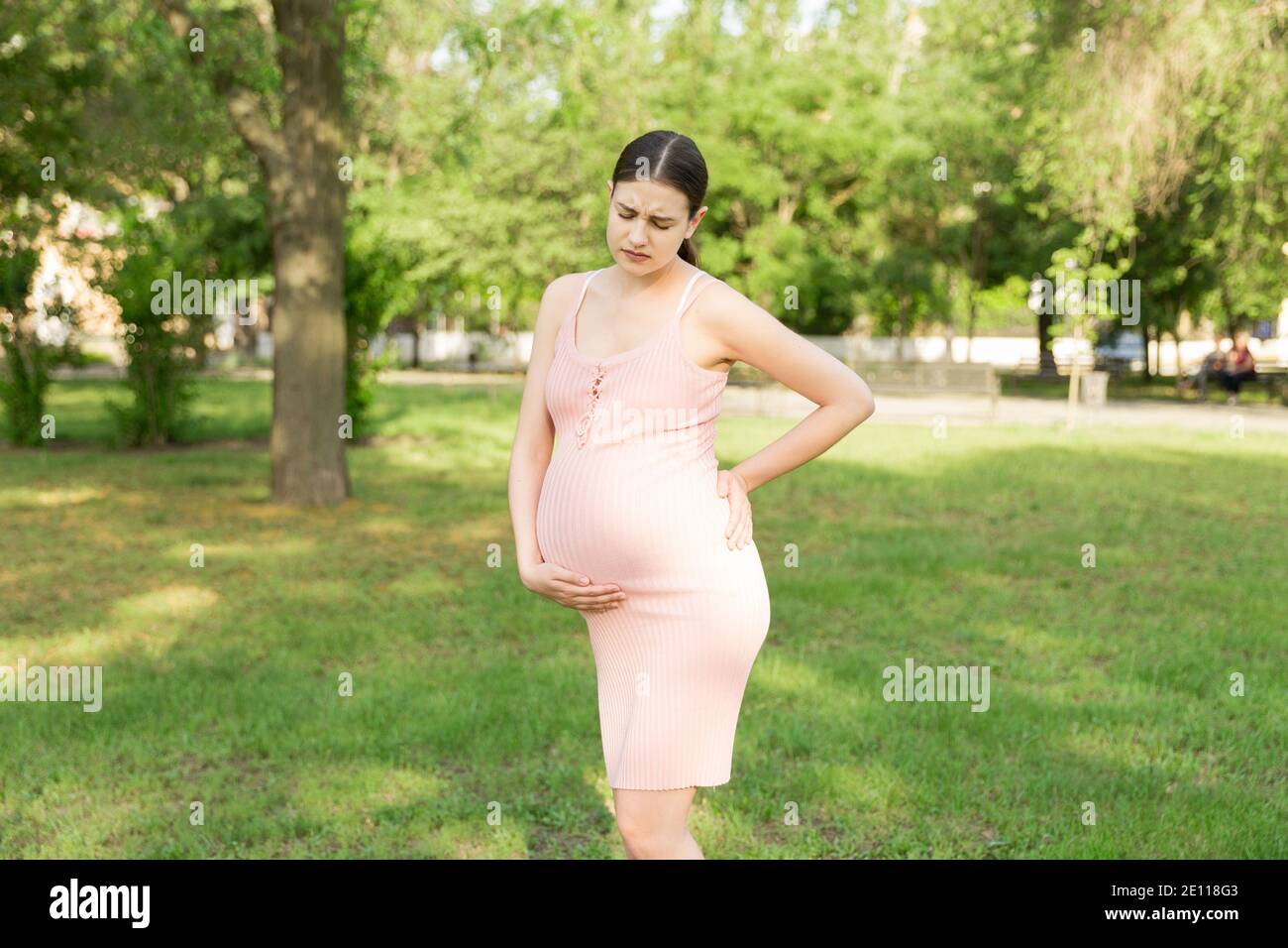 Eine schwangere junge Frau im Park und hält sich an den Magen, der schmerzt. Schwangerschaft und Mutterschaft. Rückenschmerzen während der Schwangerschaft. Stockfoto