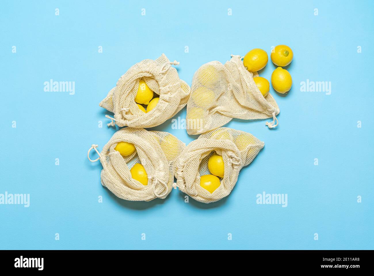 Wiederverwendbare Einkaufstaschen mit Zitronen, isoliert auf blauem Hintergrund. Draufsicht mit Zitrusfrüchten in Öko-Tüten. Nachhaltiger Lebensstil. Ethischer Konsumdenken. Stockfoto