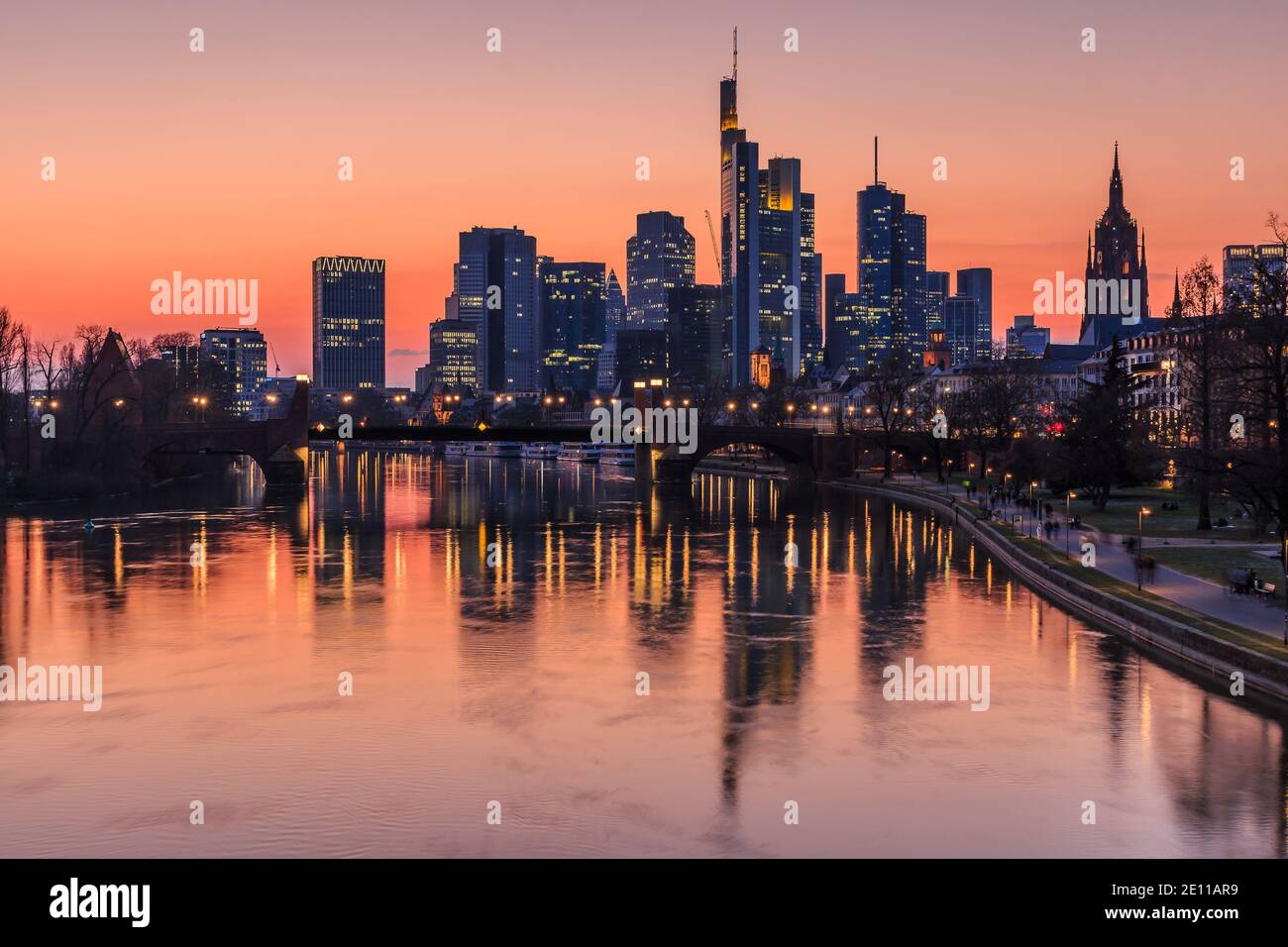 Frankfurter Skyline am Abend. Sonnenuntergang verwandelt den Himmel orange-rot. Reflexionen von beleuchteten Häusern aus dem Finanzviertel am Main Stockfoto