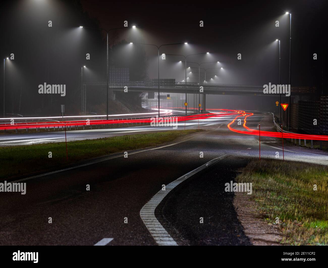 Espoo / Finnland - 1. JANUAR 2021: Straßenlaternen reflektieren an einem fuggy Abend. Leichte Wege auf der Autobahn. Stockfoto