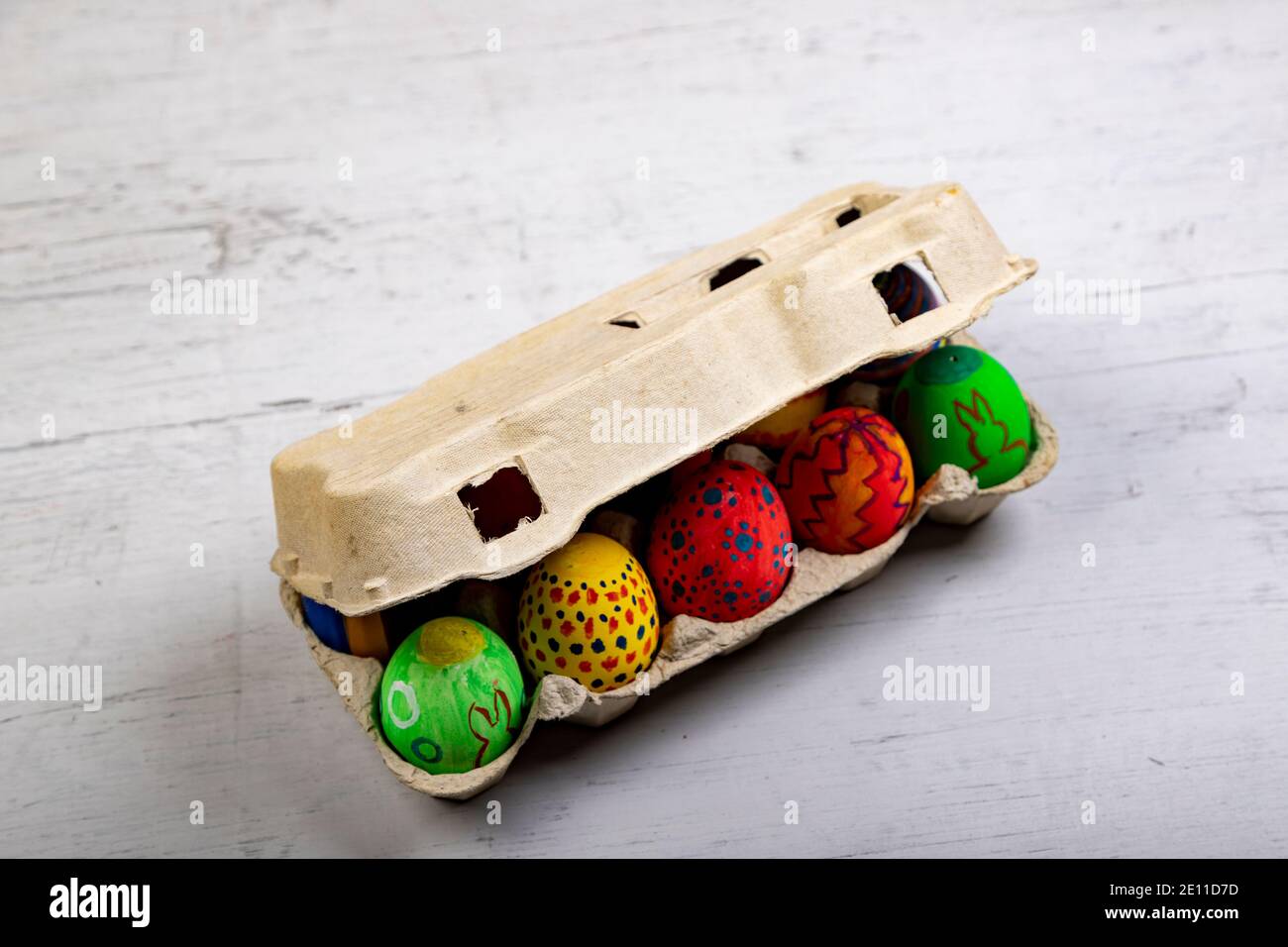 Bemalte Eier mit ostermotiven in einem geschlossenen Eierkarton Auf einem Holzbrett Stockfoto