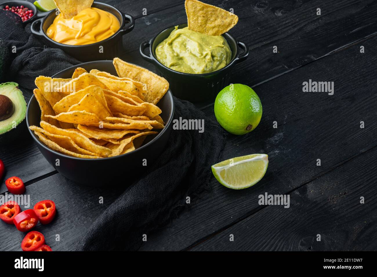 Dreieckiger gelber Mais-Tortilla-Chip mit Saucen, auf schwarzem Holzhintergrund mit Platz für Text Stockfoto
