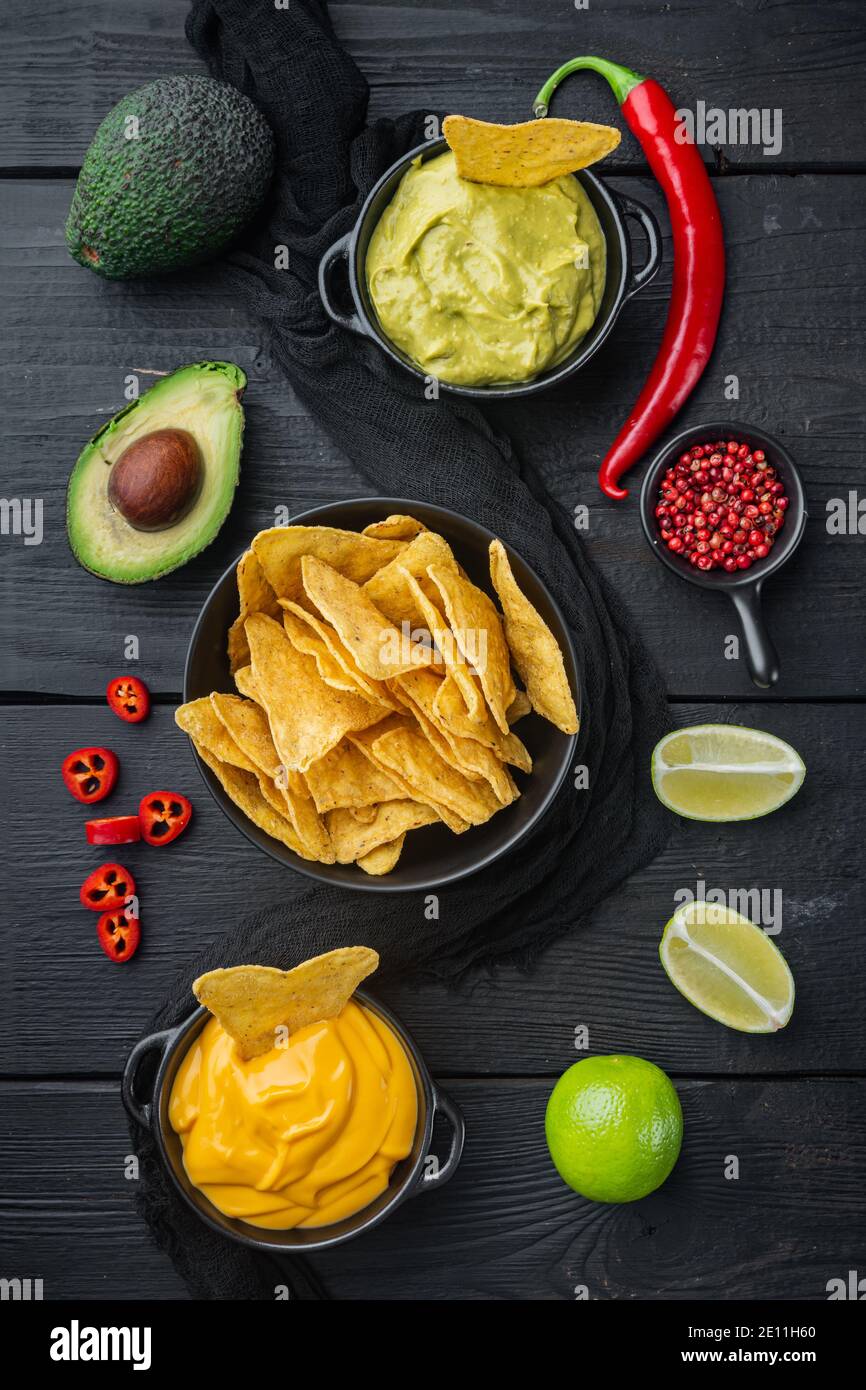 Dreieckiger gelber Mais-Tortilla-Chip mit Saucen, auf schwarzem Holzhintergrund, Draufsicht oder flaches Lay Stockfoto