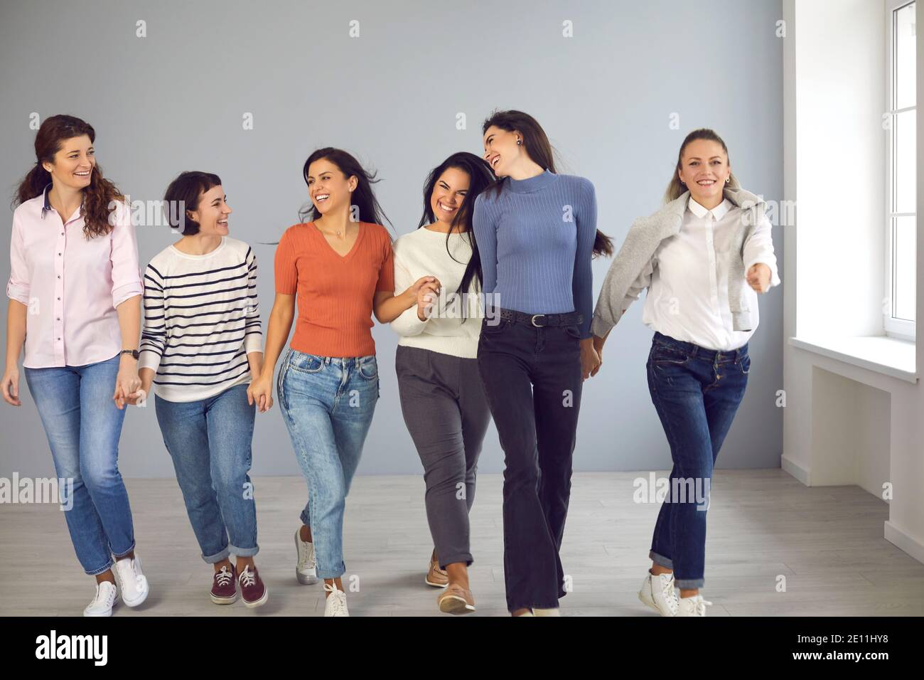 Gruppe von glücklichen schönen jungen Frauen, die zusammen gehen, Hände halten und lächeln Stockfoto
