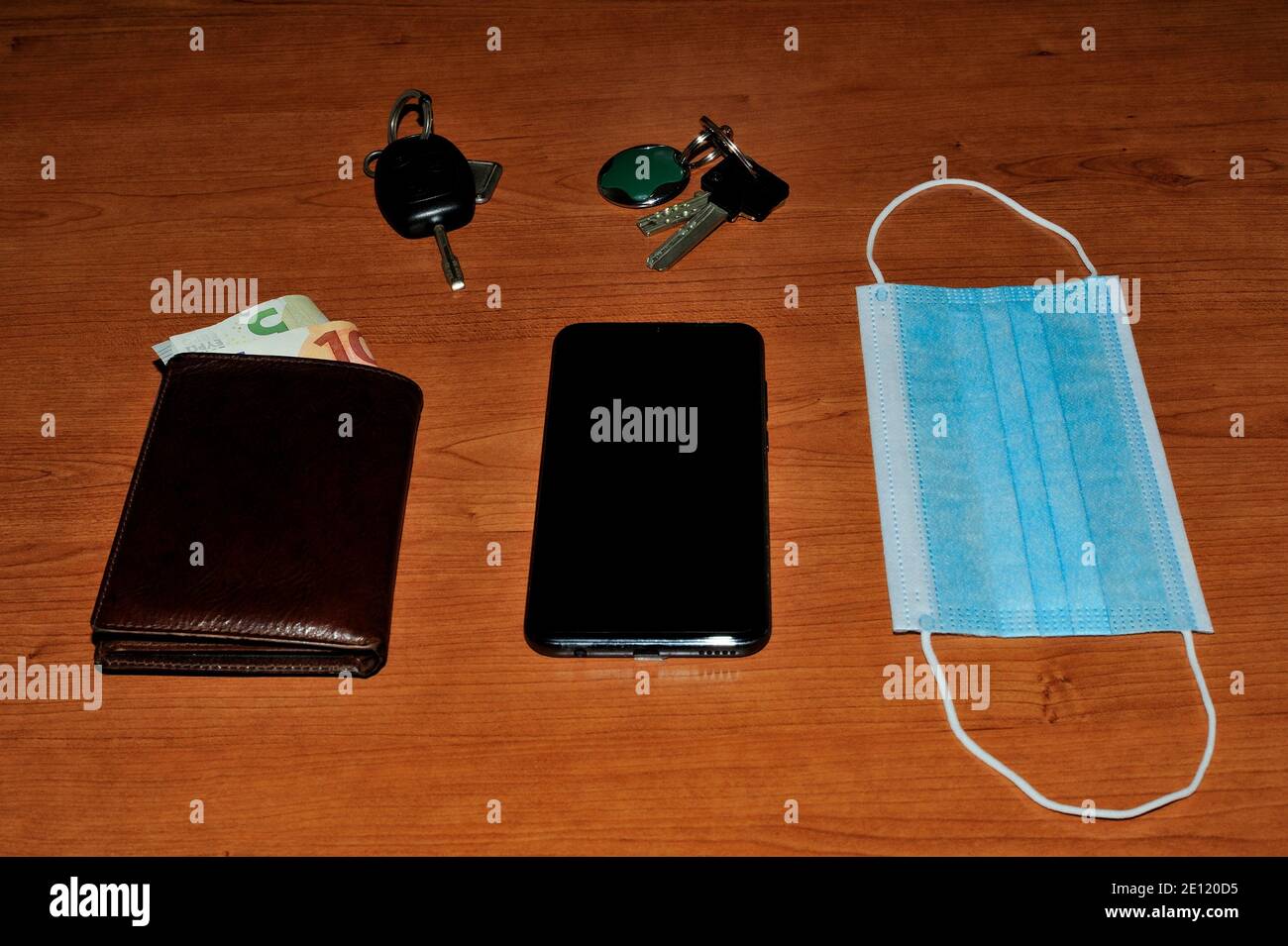 Haus- und Autoschlüssel, Geldbörse, Handy und Gesichtsmaske auf Holzfläche. Bereit, in die neue Welt zu gehen. Stockfoto