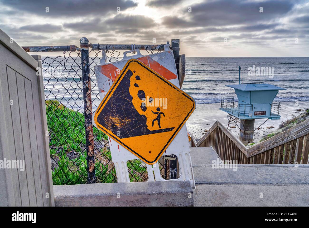 Falling Rocks Zeichen auf Treppen mit Rettungsschwimmer Turm Meer und Blick auf den bewölkten Himmel Stockfoto