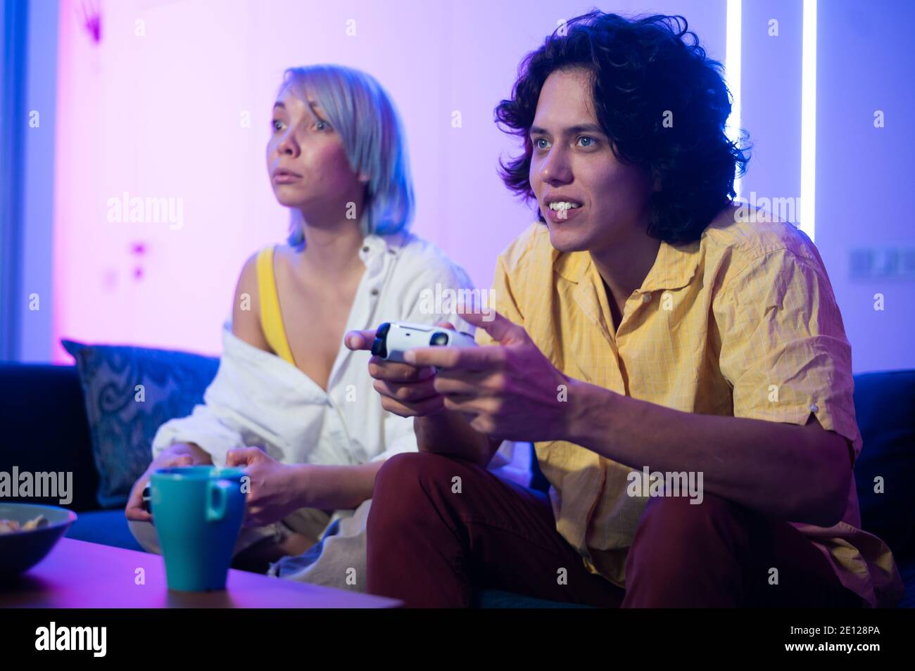 Lächelndes Paar hält Gamepads spielen Videospiel zu Hause. Low-Angle-Aufnahme junger Menschen, die während der Selbstisolation gegen Pandemie Zeit miteinander verbringen. Stockfoto