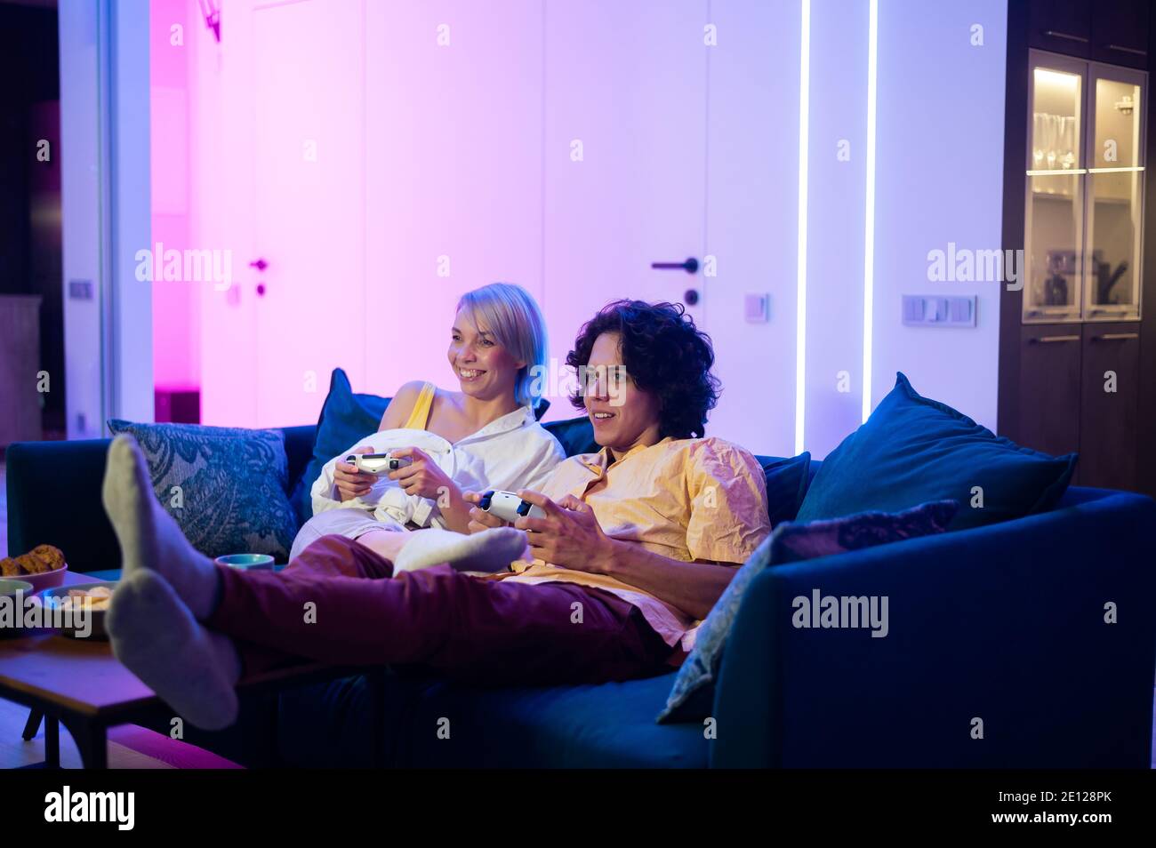 Glückliches junges Paar, das ein Videospiel spielt, das zu Hause auf einem Sofa während der Selbstisolierung in Quarantäne sitzt. Stockfoto