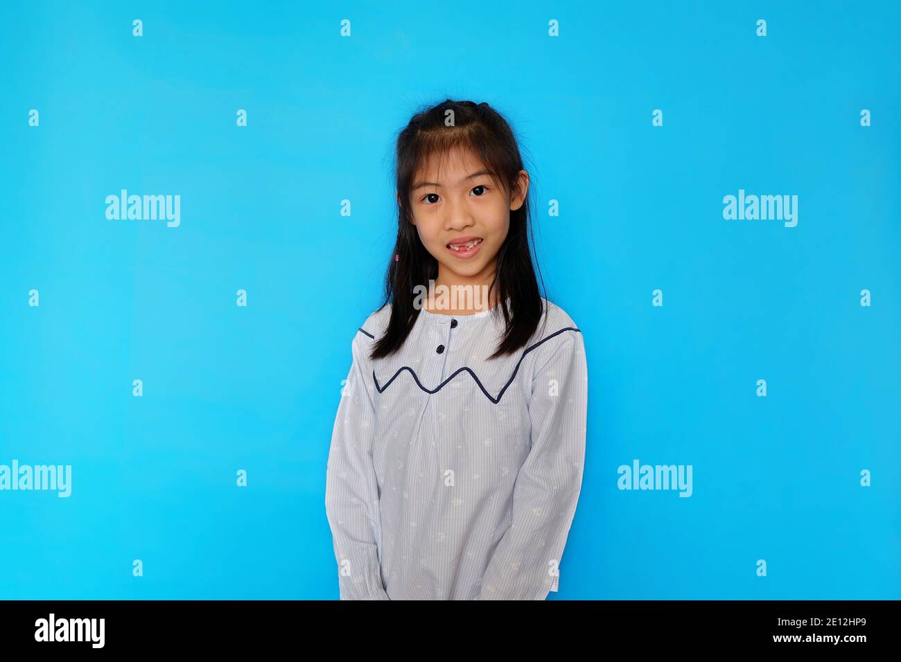 Ein nach vorne gerichtetes Porträt eines attraktiven asiatischen präteen Mädchen, das vor einem hellblauen Hintergrund steht und lächelt. Stockfoto