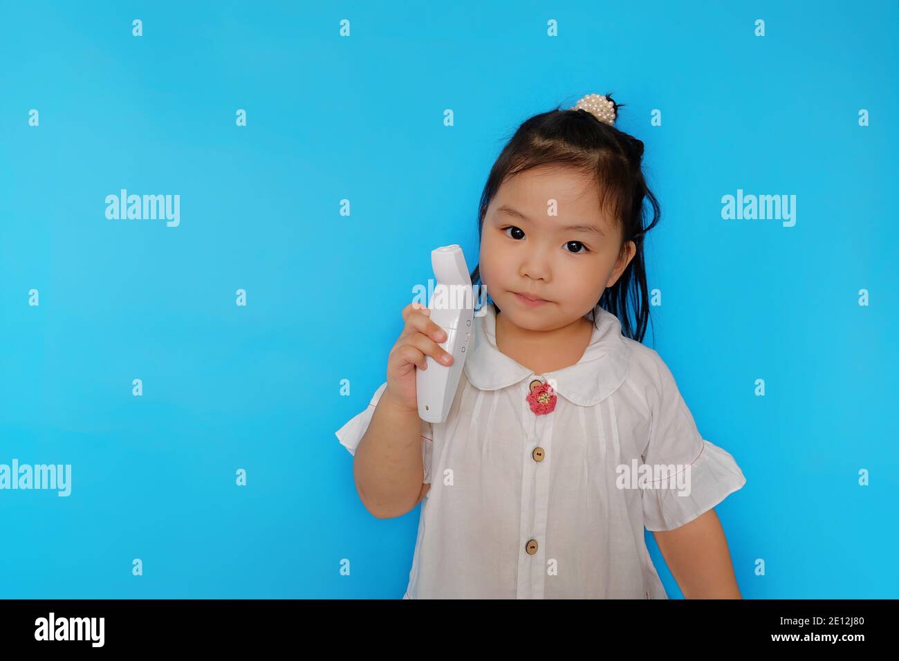 Ein nettes junges asiatisches Mädchen ist Rollenspiel als Arzt, hält ein Infrarot-Thermometer versucht, die Temperatur ihrer Familienmitglieder zu überprüfen, suchen Stockfoto