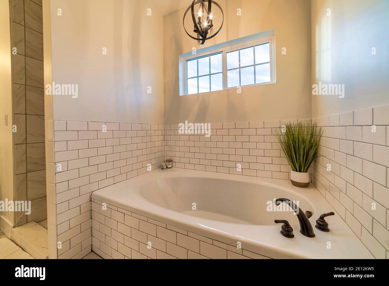 Eingebaute ovale Badewanne mit schwarzem Wasserhahn gegen weiße Fliesen Wand des Badezimmers Stockfoto