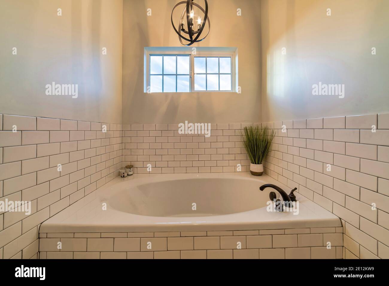 Runde eingebaute Badewanne im Badezimmer mit weiß gefliesten Wänden Und ein kleines Fenster Stockfoto