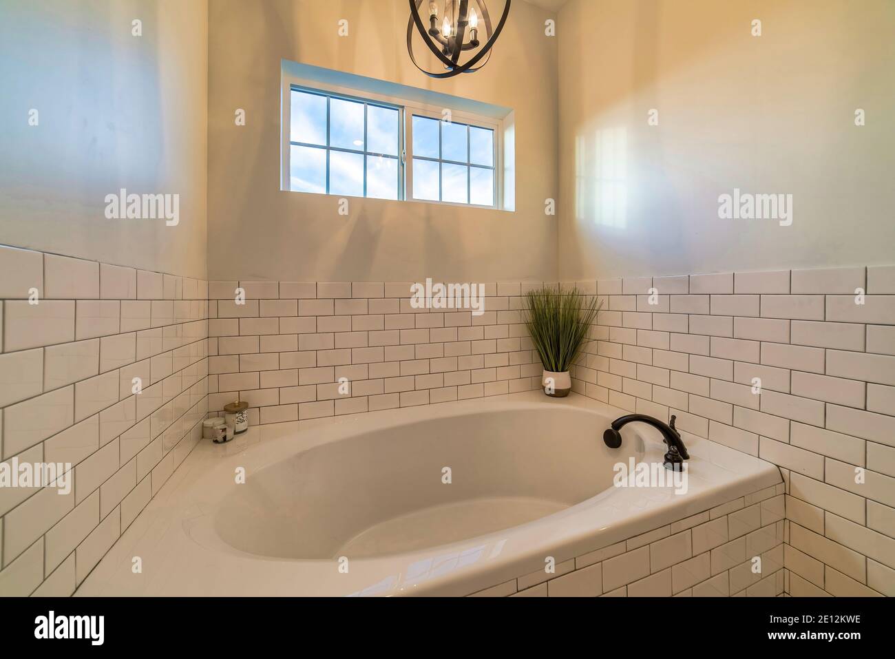 Eingebaute runde Badewanne mit Hängeleuchte im Badezimmer mit Geflieste Wand Stockfoto