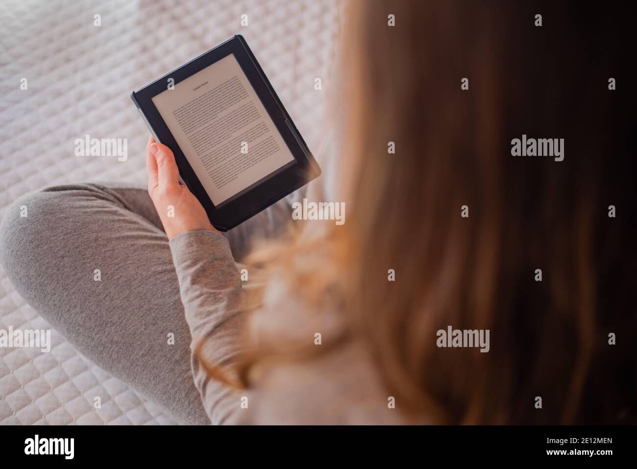 Frau liest E-Book auf dem Bett sitzend. Konzept für Studium, Lesen Stockfoto