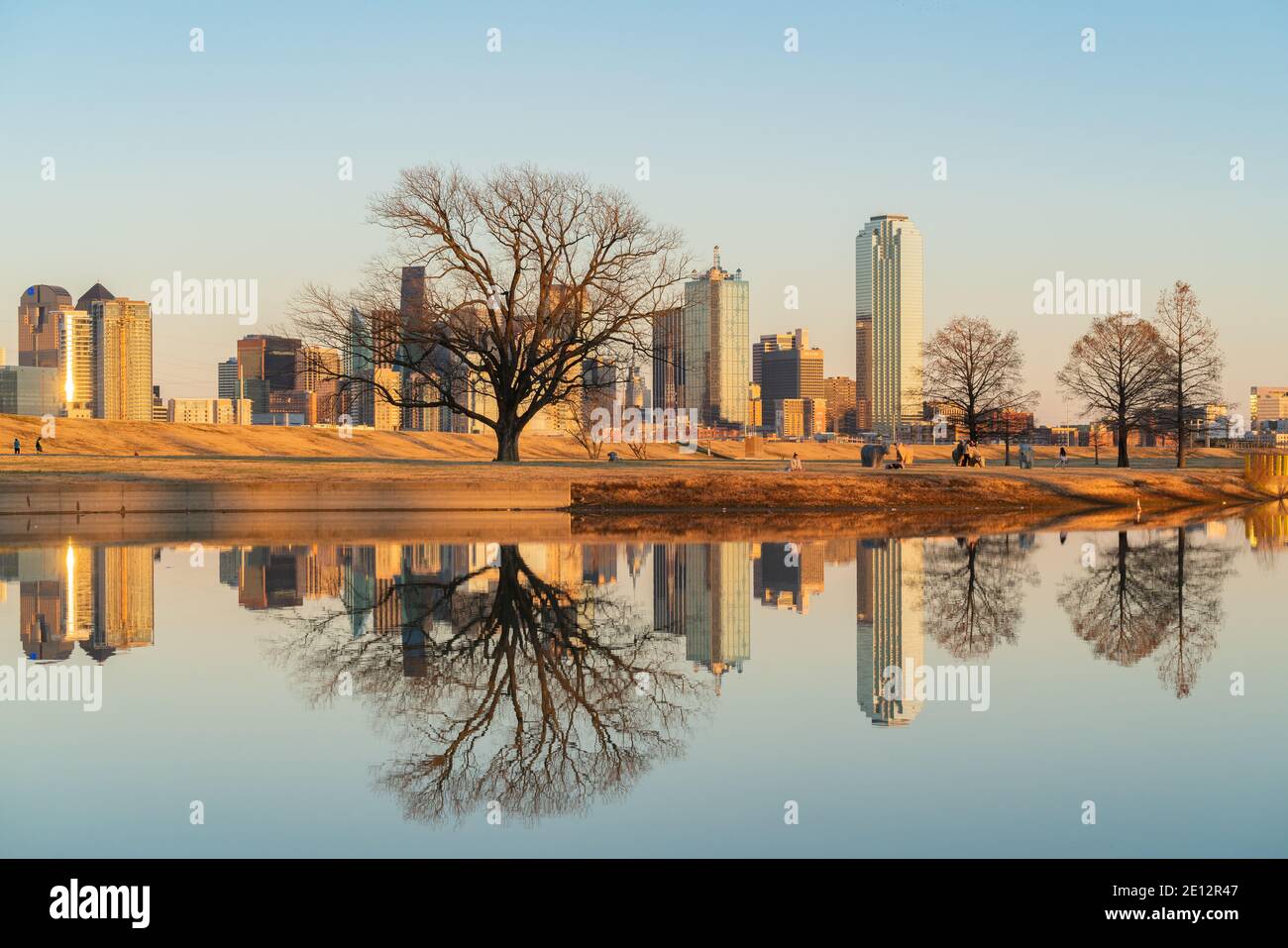 Menschen entspannen im Trammel Crow Park mit Blick auf die Skyline von Dallas, Texas im Hintergrund und reflektierenden Teich im Vordergrund. Stockfoto