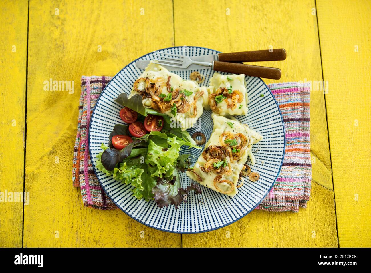 Schwäbische Ravioli mit gerösteten Zwiebeln und runny Käse, serviert mit Salat auf EINEM Gelben Holztisch Stockfoto