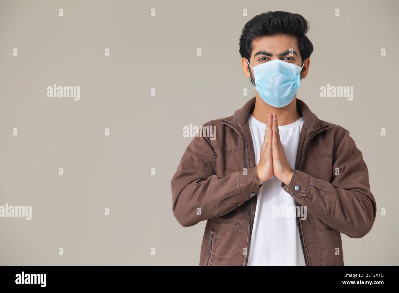 EIN JUNGER MANN TRÄGT MASKE GRUSS MIT GEFALTETEN HÄNDEN Stockfoto