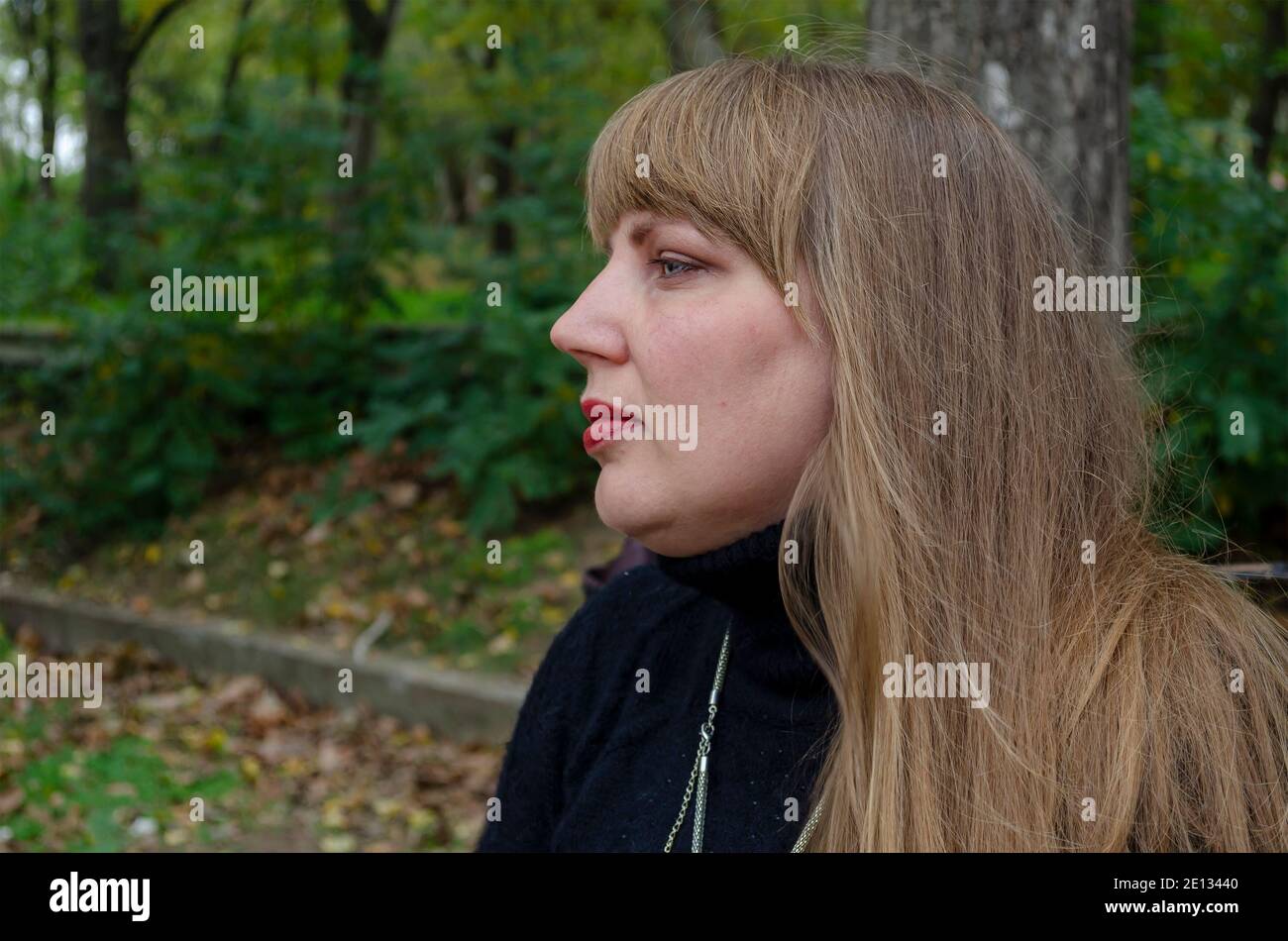 Frau mittleren Alters mit langen lockeren Haaren im Hintergrund des grünen Parks. Seitenansicht. Minimale Fotobearbeitung Stockfoto