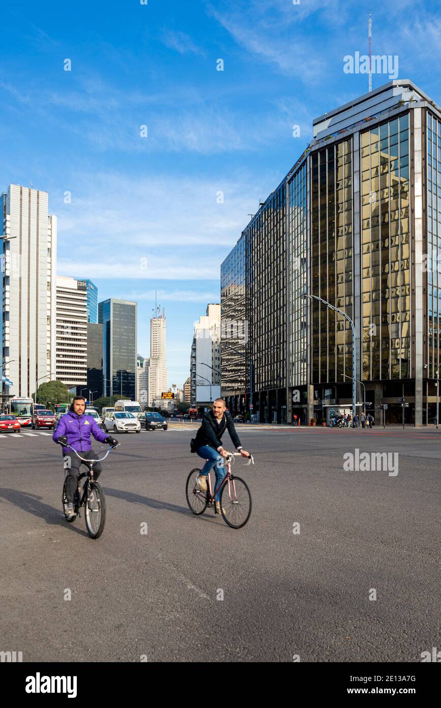 Buenos Aires, Retiro Finanzviertel. Zwei Männer auf dem Fahrrad überqueren eine leere Straße, Geschäftsgebäude im Hintergrund Stockfoto