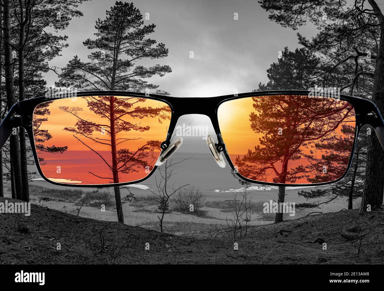 Unterschiedliche Wahrnehmung der Welt. Farbenfrohe Sicht auf den Sonnenuntergang über Meer und Nadelwald in den Gläsern. Durch die Brille schauen. Stockfoto