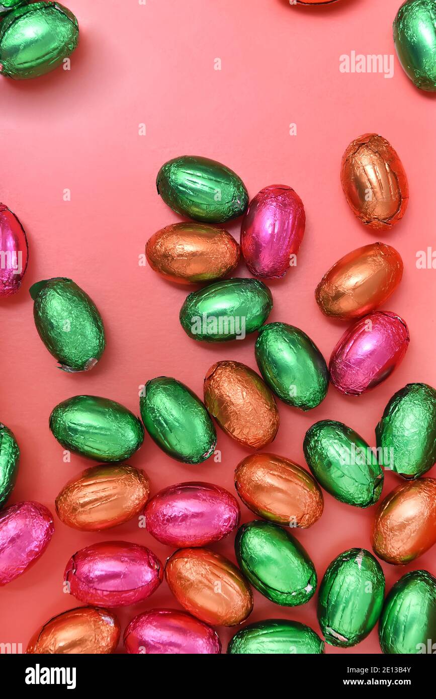 Große und kleine bunte rosa, grün, orange und Gold Folie verpackt Schokolade Mini ostereier, vor einem pfirsichorange Hintergrund. Stockfoto