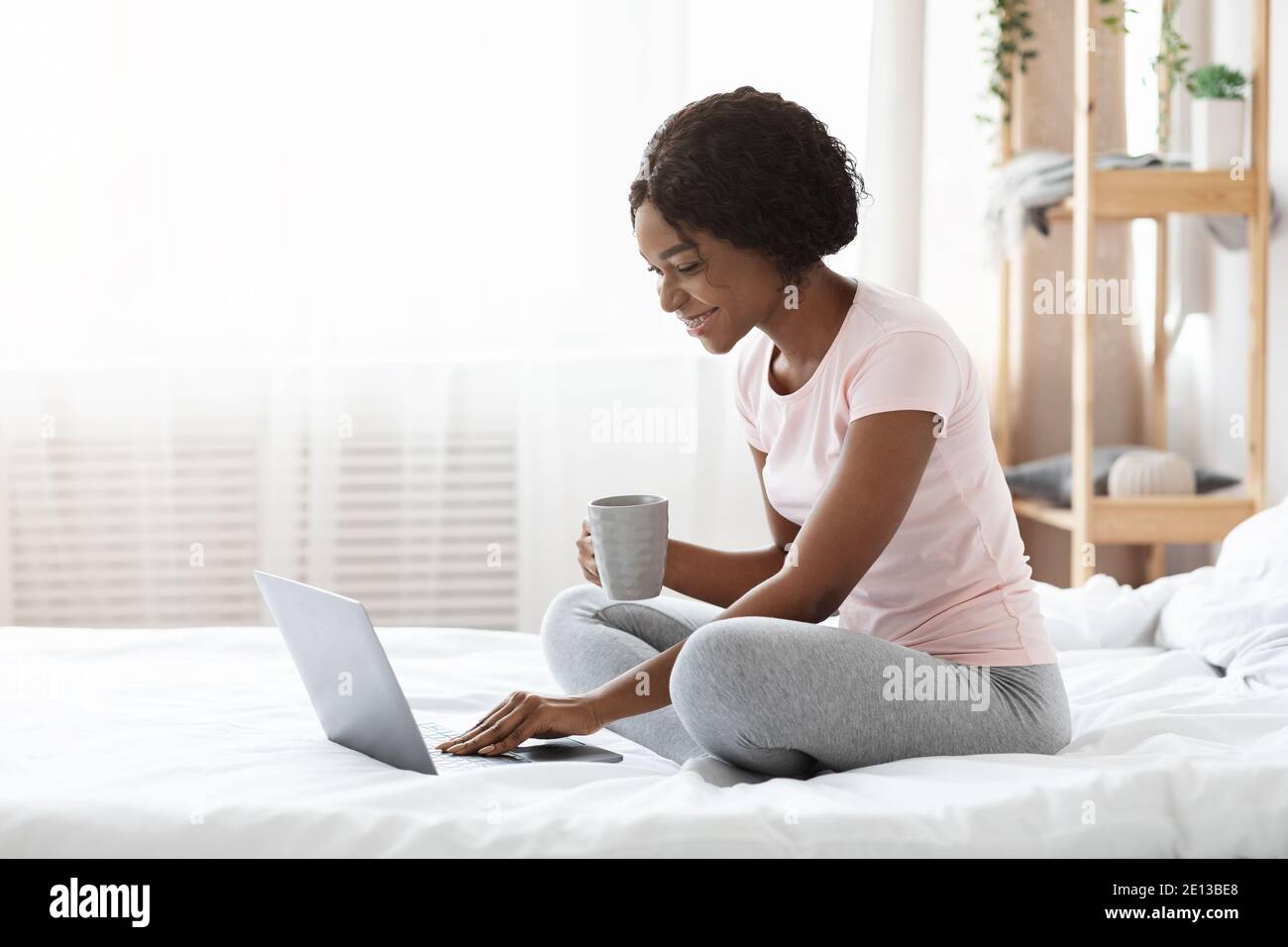 Glückliche Frau mit einer Tasse Tee mit Laptop im Bett Stockfoto