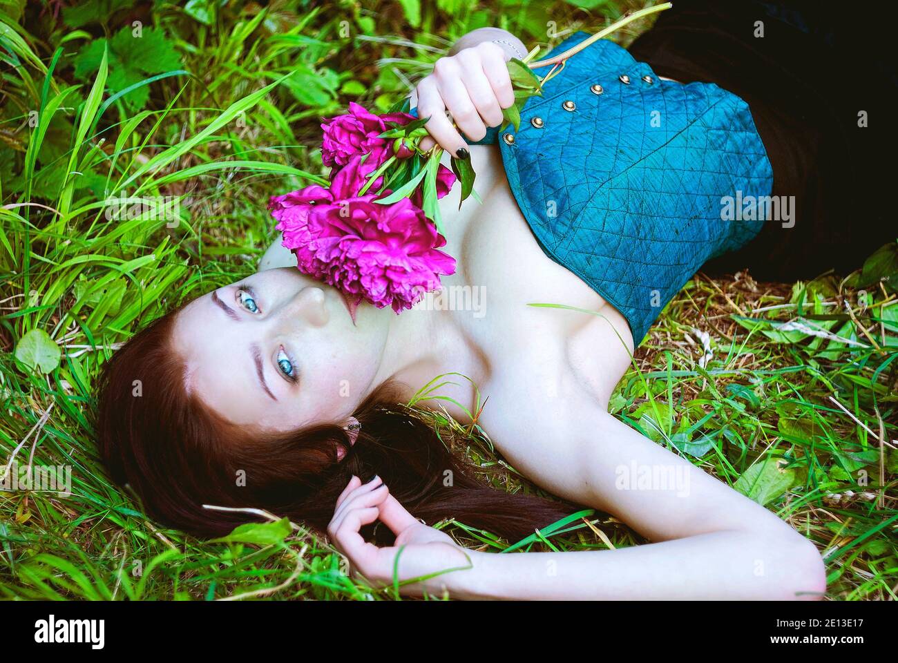 Porträt einer jungen attraktiven Frau im Frühlingsgarten mit blühenden rosa Pfingstrosen. Federhintergrund. Frauentag. Grußkarte. Stockfoto